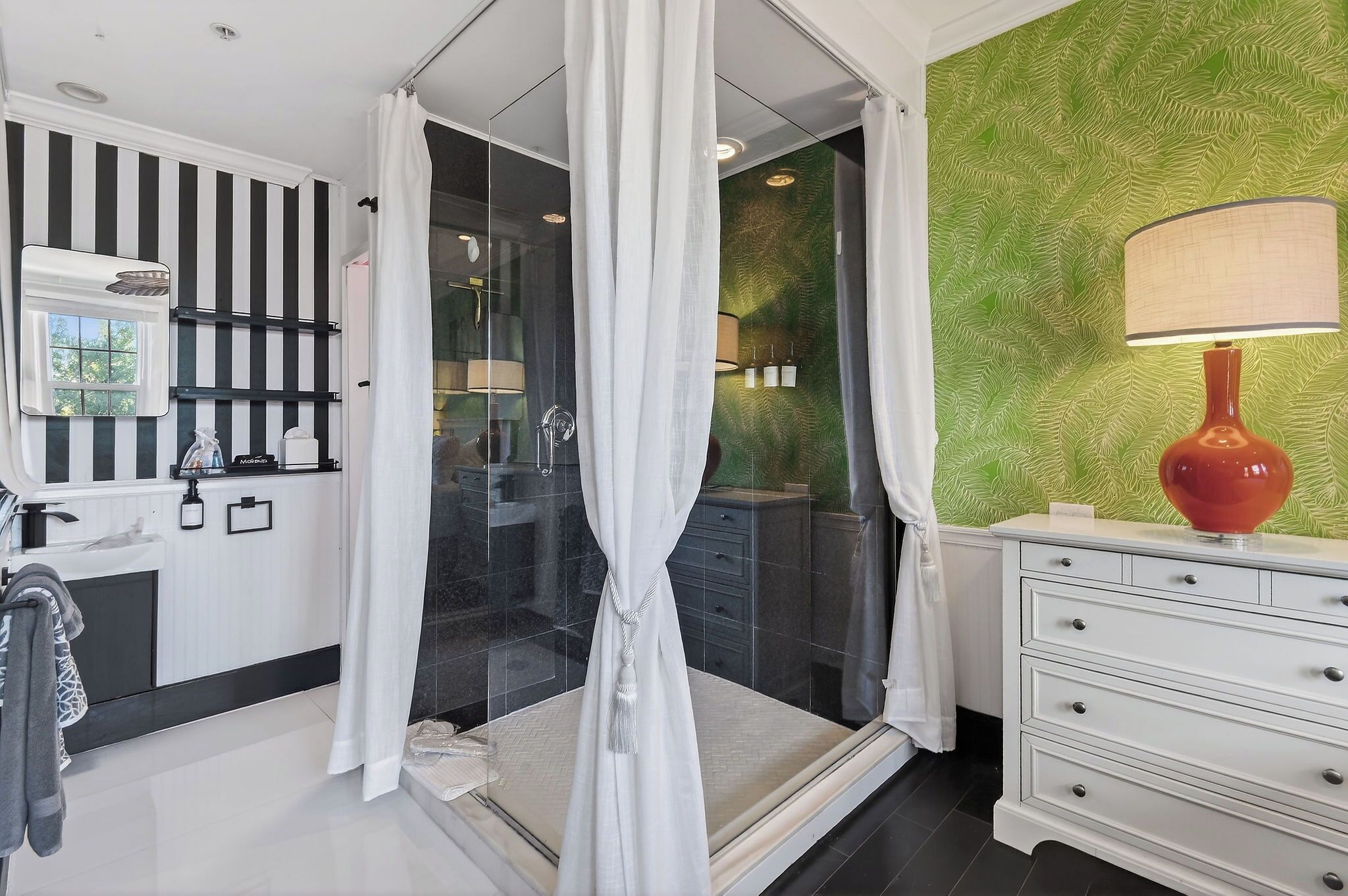 Casa de banho moderna com cabine de chuveiro em vidro, toucador branco com uma lâmpada vermelha e parede com padrão verde.