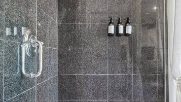 A modern shower area with dark tiles, a glass door, and three bottles of shampoo.