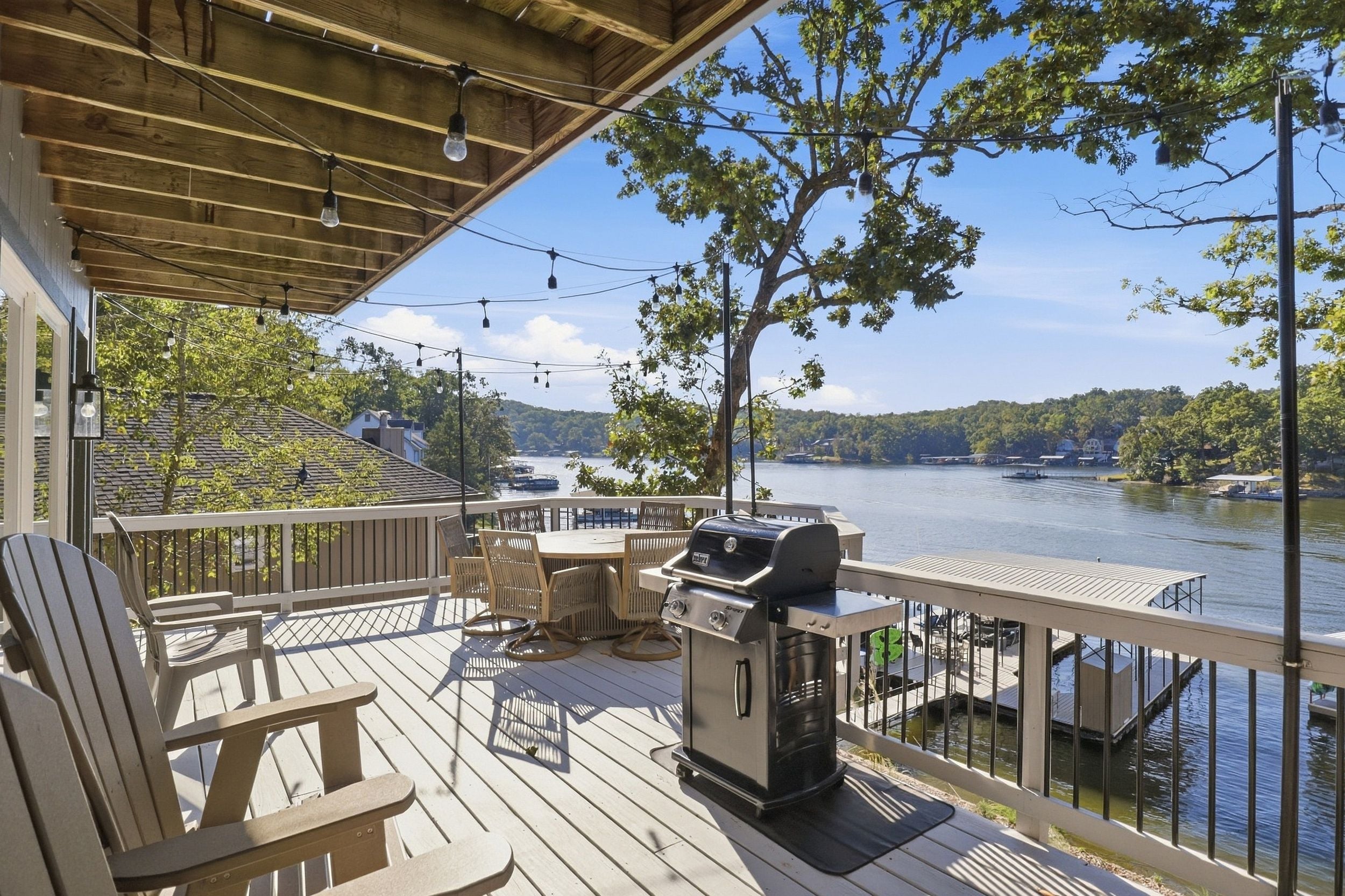 A wooden deck with outdoor furniture, a grill, and a view of a lake with boats.