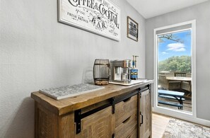 A kitchen counter with a coffee and cocktail sign, a bar sign, and a window with a view of a deck and trees.