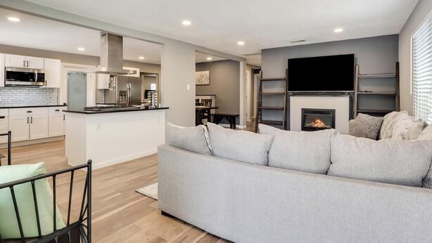 A modern living room with a grey sofa, a flat-screen TV mounted on the wall, and a fireplace.