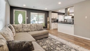 A modern living room with a sectional sofa, a green door, and a kitchen in the background.
