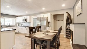 A modern kitchen with white cabinets, a large island, and a dining area with a wooden table and chairs.