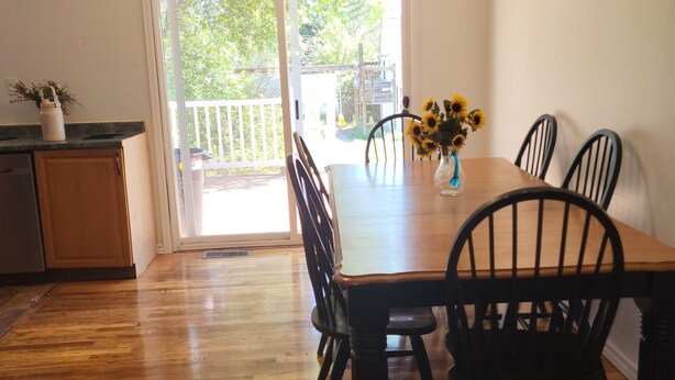 Uma sala de jantar com mesa e cadeiras de madeira, ventilador de teto e vista para um deck externo através de uma porta de vidro.