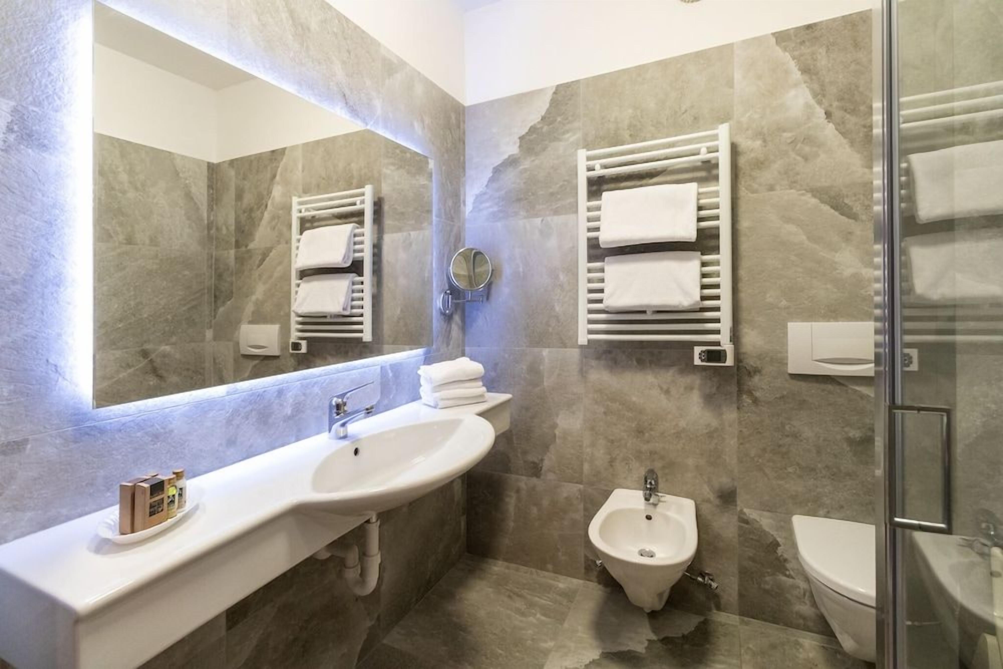 Une salle de bain moderne avec un grand miroir, un lavabo, un bidet et des porte-serviettes.