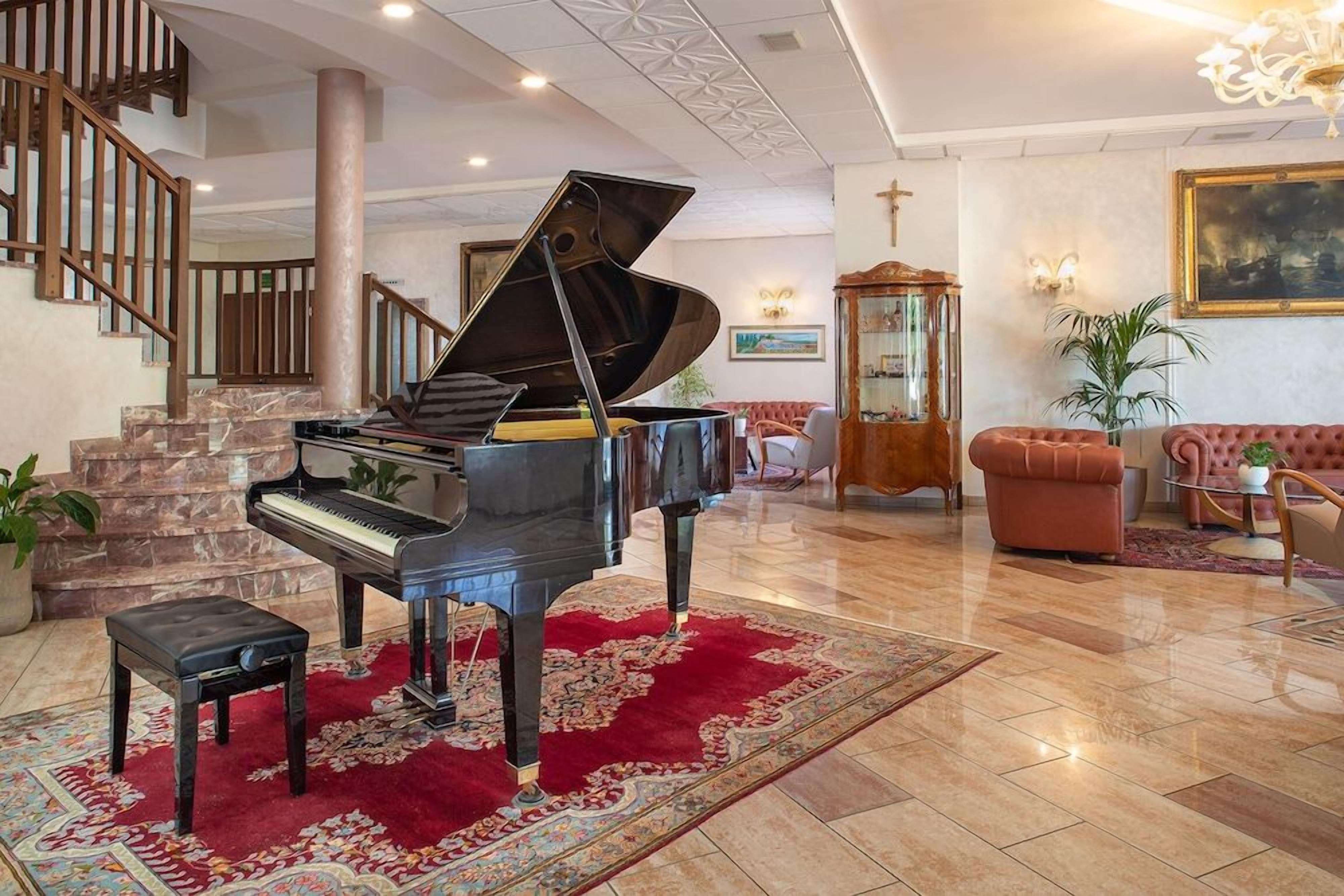 A grand piano in a spacious lobby with a red carpet, a staircase, and a classic chandelier.