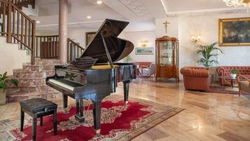 A grand piano in a spacious lobby with a red carpet, a staircase, and a classic chandelier.