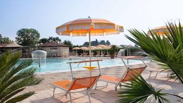 A pool area with lounge chairs and umbrellas, a water feature, and a stone structure.
