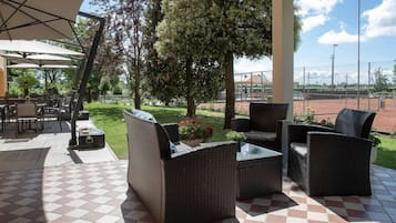 An outdoor patio with wicker furniture, a tennis court in the background, and a clear sky.