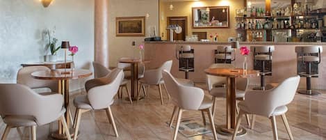 A hotel bar area with round tables and chairs, a bar counter with a mirror, and a wall of liquor bottles.
