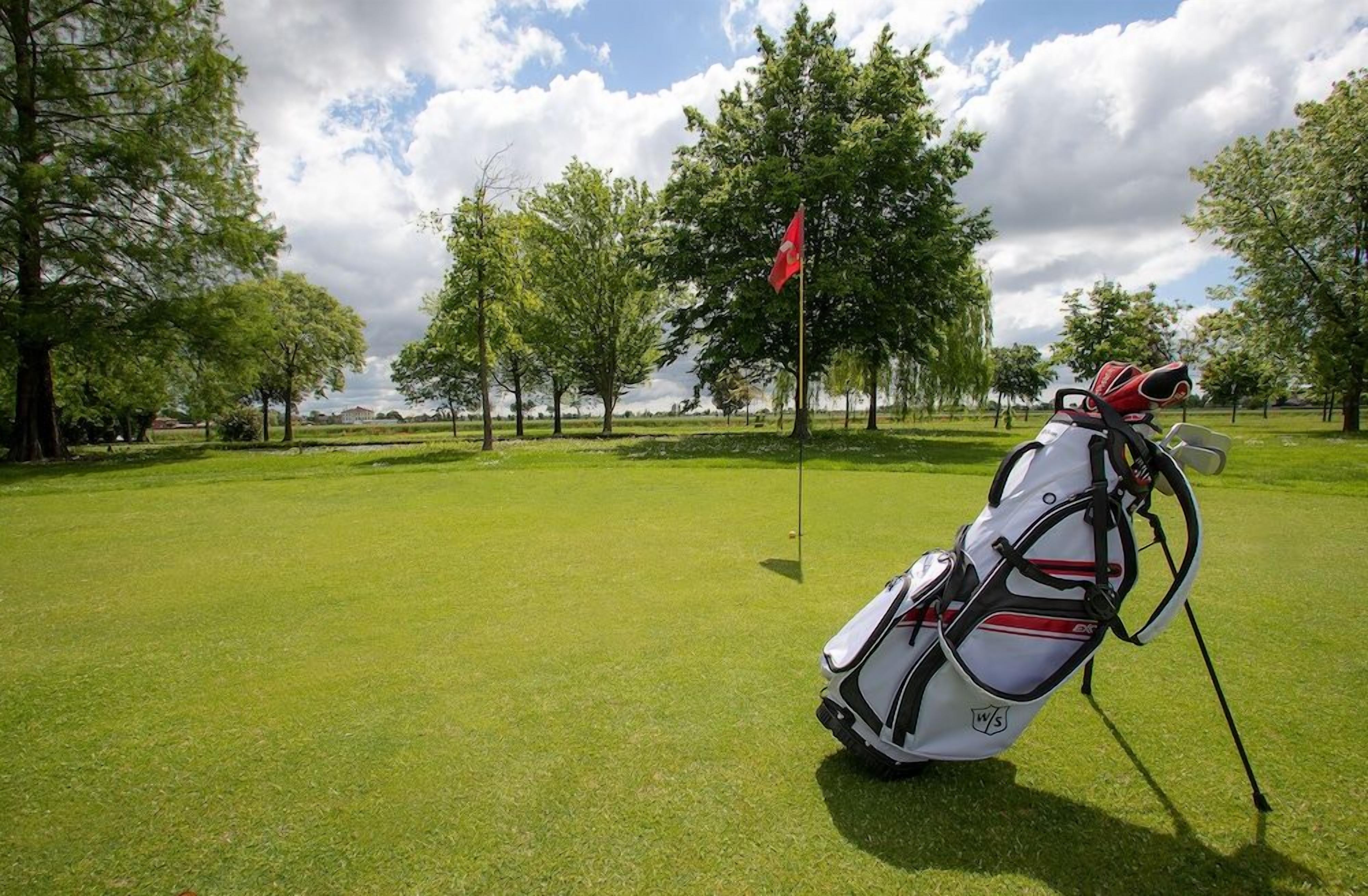 Una borsa da golf su un prato verde curato, con un’asta di bandiera in lontananza.