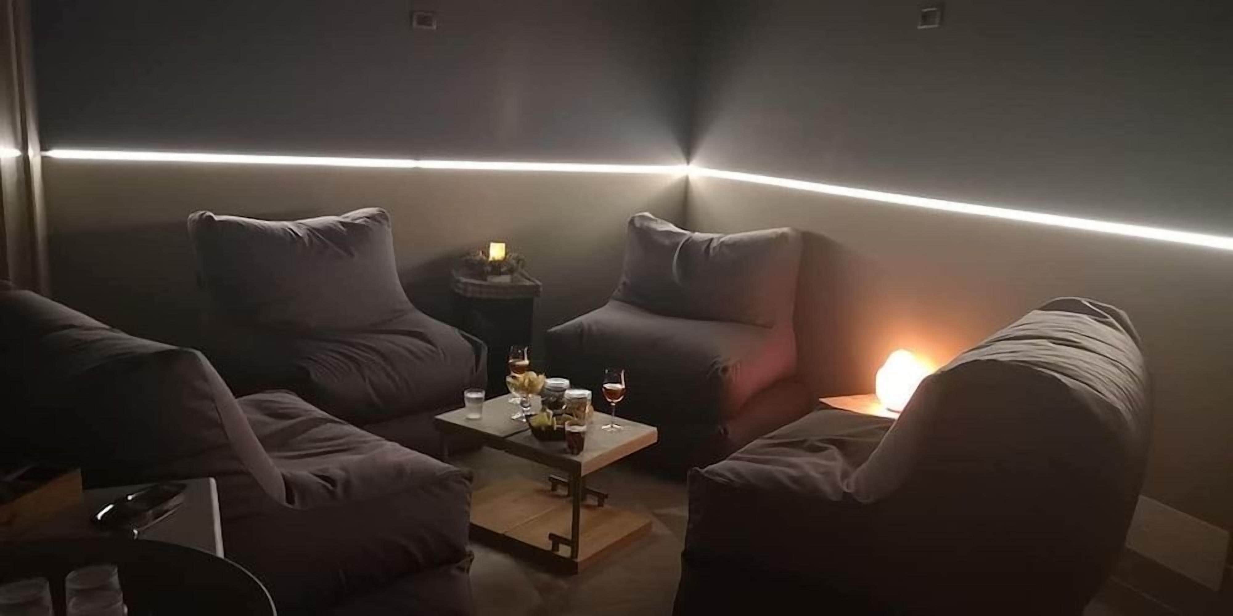 A dimly lit room with a modern design, featuring a sofa set, a small table with drinks, and a wall-mounted light fixture.