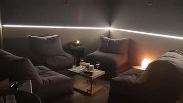 A dimly lit room with a modern design, featuring a sofa set, a small table with drinks, and a wall-mounted light fixture.