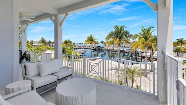 A covered outdoor seating area with a view of a marina and palm trees. - Luxury Waterfront Home - Marathon, FL Keys - 5BR, Private Pool, Dock - Sleeps 10 (Marathon)