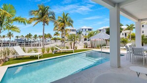A pool area with a view of the marina and palm trees, surrounded by white buildings. - Luxury Waterfront Home - Marathon, FL Keys - 5BR, Private Pool, Dock - Sleeps 10 (Marathon)