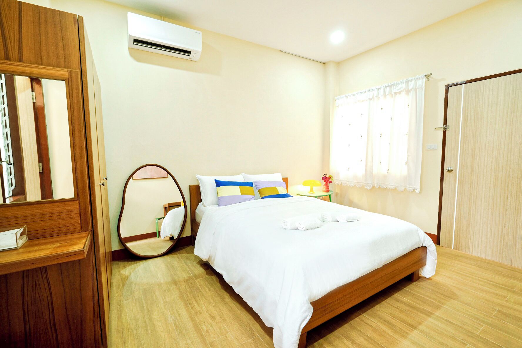 Habitación de hotel con cama de madera, espejo redondo, mesita de noche con lámpara y ventana con cortinas.