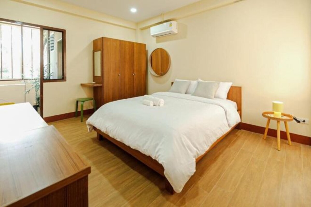 Une chambre avec un grand lit, une armoire en bois, un miroir rond et une petite table sur laquelle est posée une bougie.