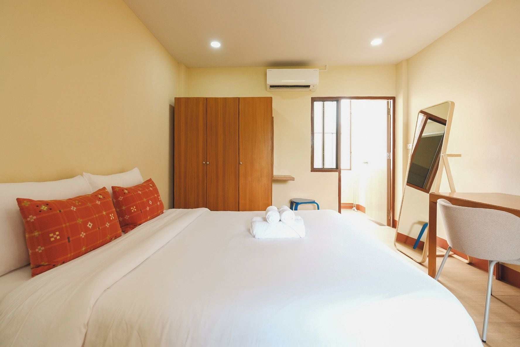 A hotel room with a bed, a wooden wardrobe, a desk with a chair, and a window.