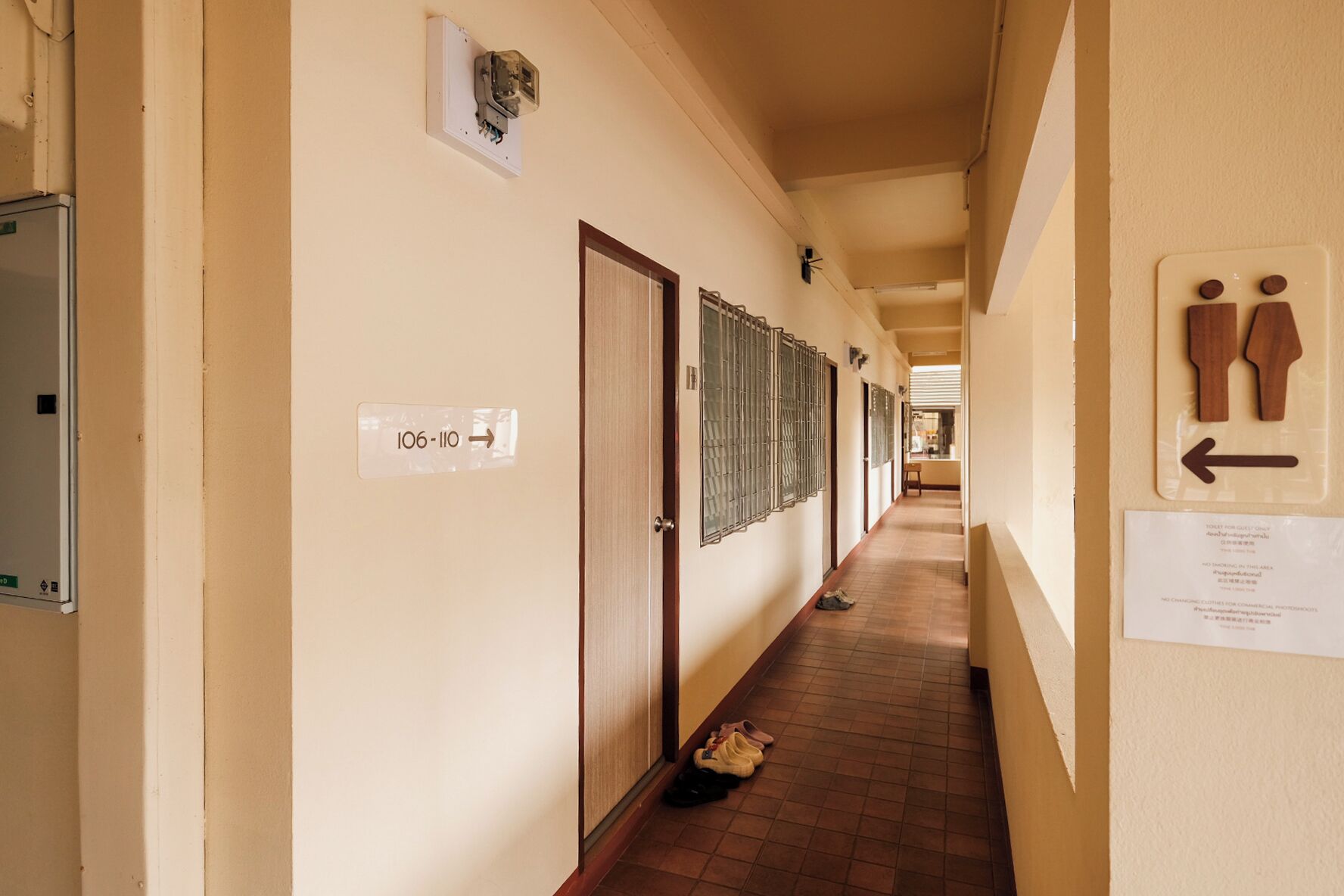 A hallway with doors labeled '106-110', a trash bin, and a wall-mounted sign with a restroom symbol.