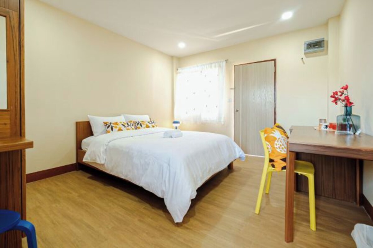 Une chambre à coucher avec un lit, un bureau en bois, une chaise et une fenêtre avec des rideaux.