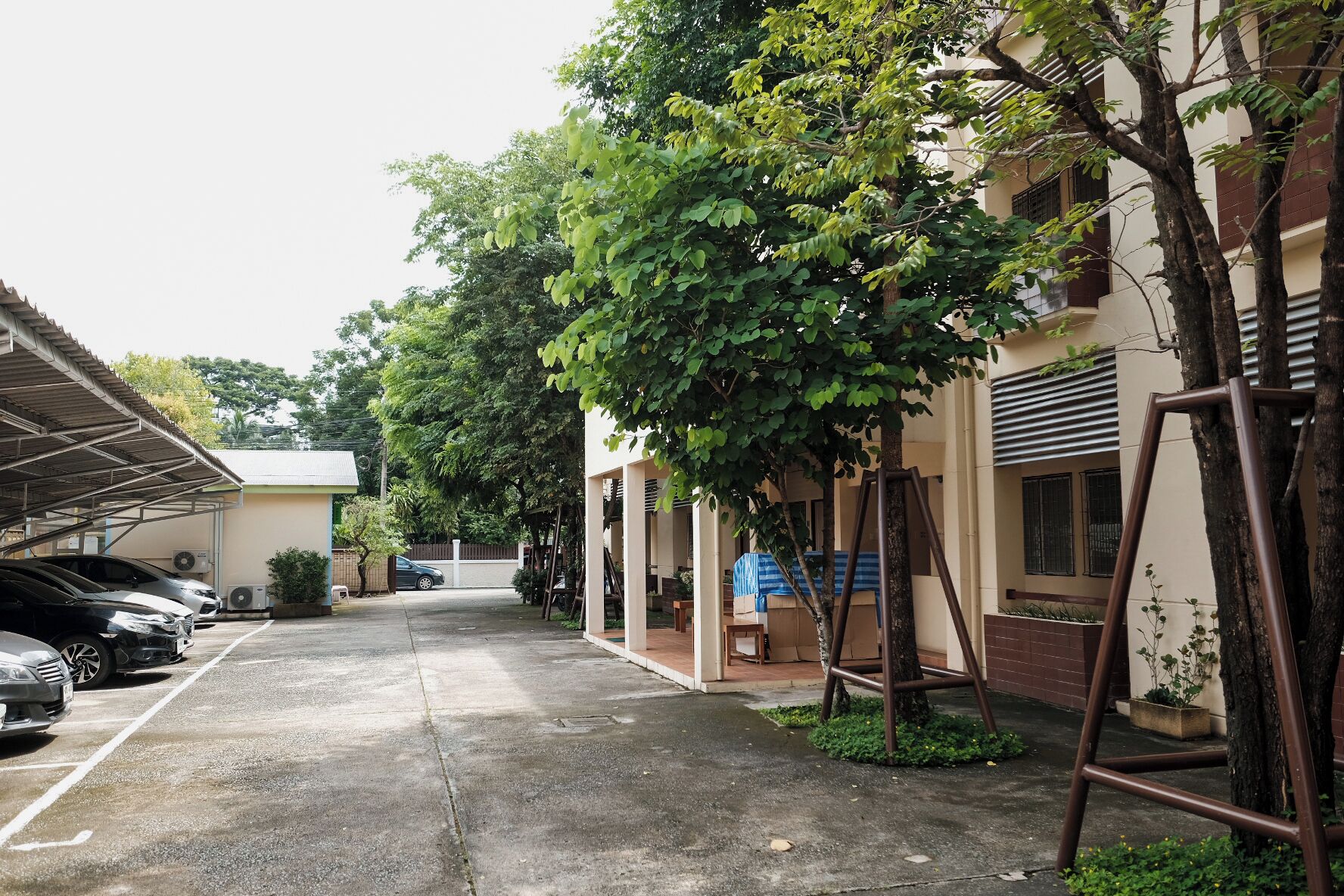 A parking area with cars, a covered walkway, and a building with a swing set.