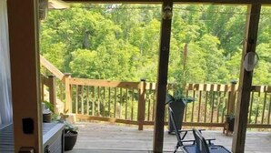 An outdoor patio area with a covered seating area, a grill, and a view of a wooded area.