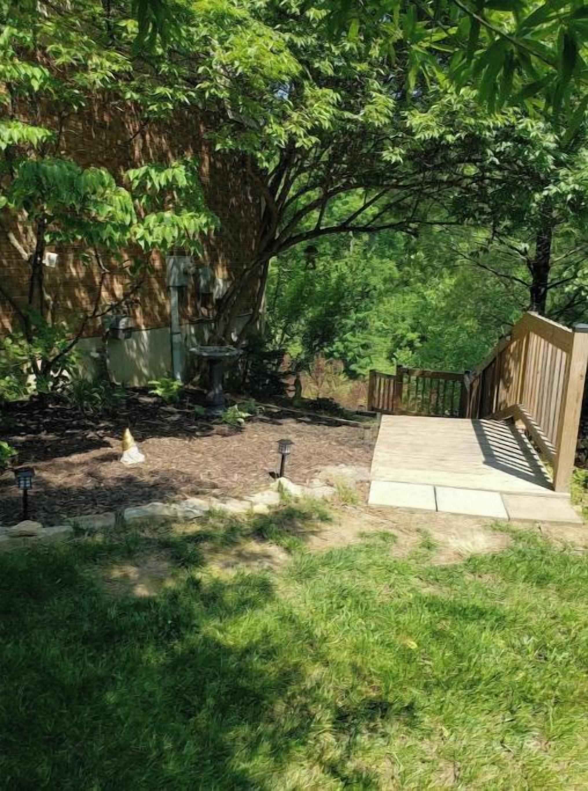 A backyard with a wooden deck, a stone wall, and a large tree providing shade.