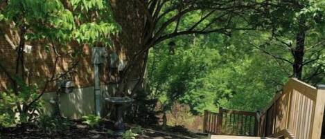 A backyard with a wooden deck, a stone wall, and a large tree providing shade.
