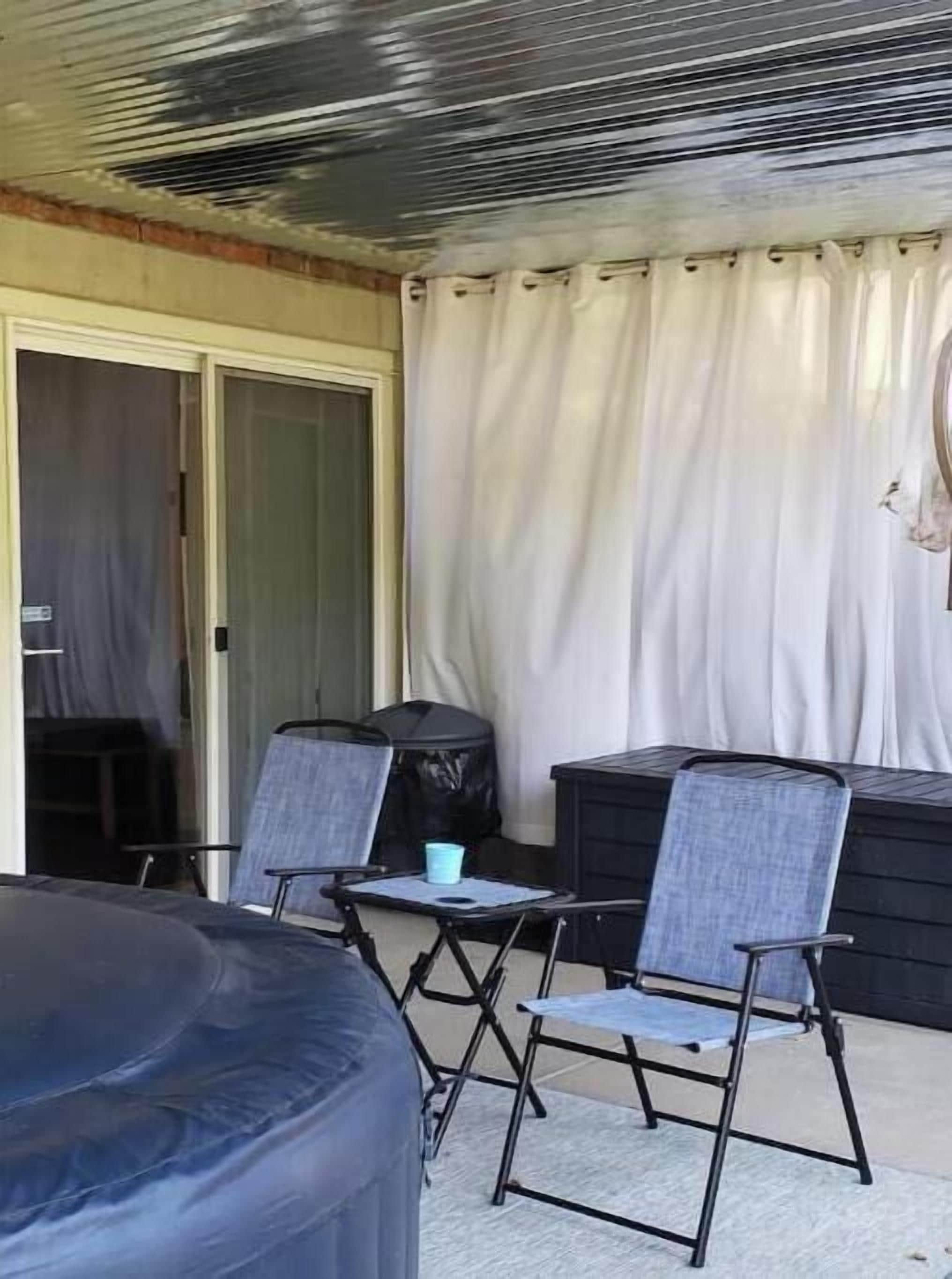 A covered outdoor seating area with a table and chairs, a black storage unit, and a door leading to another room.