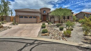 A residential house with a stone facade, a tiled roof, and a landscaped front yard with various plants and rocks.
