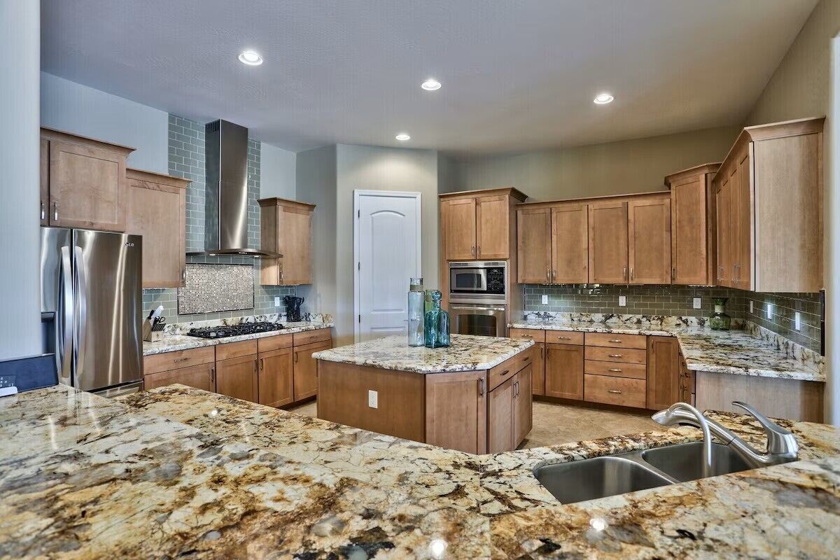 A modern kitchen with granite countertops, stainless steel appliances, wooden cabinets, and a central island.