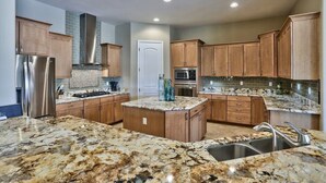 A modern kitchen with granite countertops, stainless steel appliances, wooden cabinets, and a central island.