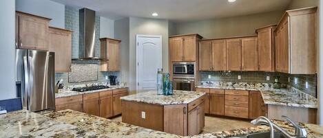 A modern kitchen with granite countertops, stainless steel appliances, wooden cabinets, and a central island.