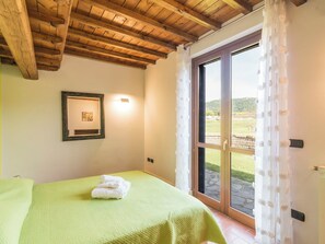 Quarto com cama, um quadro na parede e vista através de uma porta de vidro.