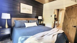 Un dormitorio con una cama grande, dos mesitas de noche con lámparas, un cabecero de madera y un cuadro en la pared.