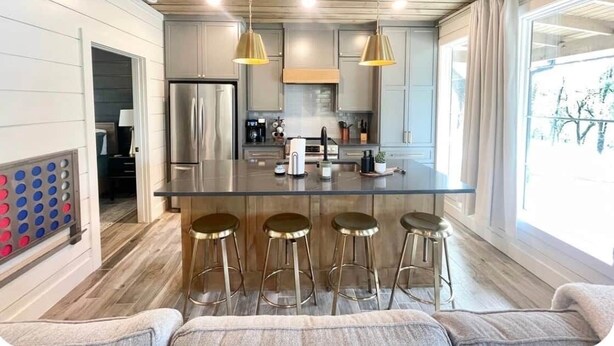 Una cocina moderna con una isla central, taburetes de bar, iluminación colgante y un ventanal grande.