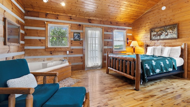 A log cabin bedroom with a wooden bed, a bench, a bathtub, and a window with blinds. - 21 Acre Mountain Escape!  11 Private Cabins!  Weddings, Reunions, & Events! (Fancy Gap)