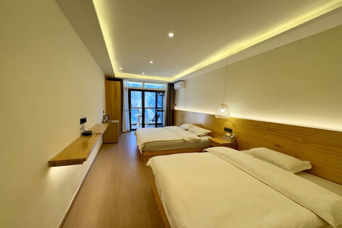 Een hotelkamer met twee bedden, een houten bureau, een stoel en een groot raam met uitzicht.