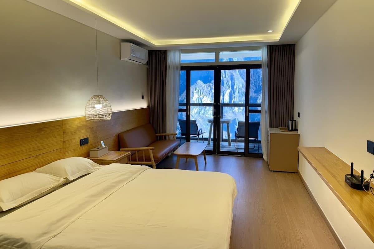 Een hotelkamer met een bed, een zithoek met een tafel, een bureau en uitzicht op bergen door grote ramen.