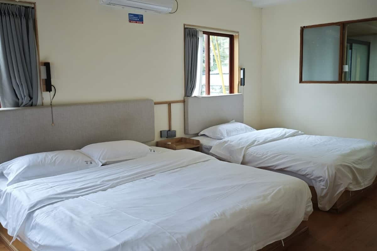Een hotelkamer met twee bedden, een raam met gordijnen, een airconditioningsunit en een houten nachtkastje.