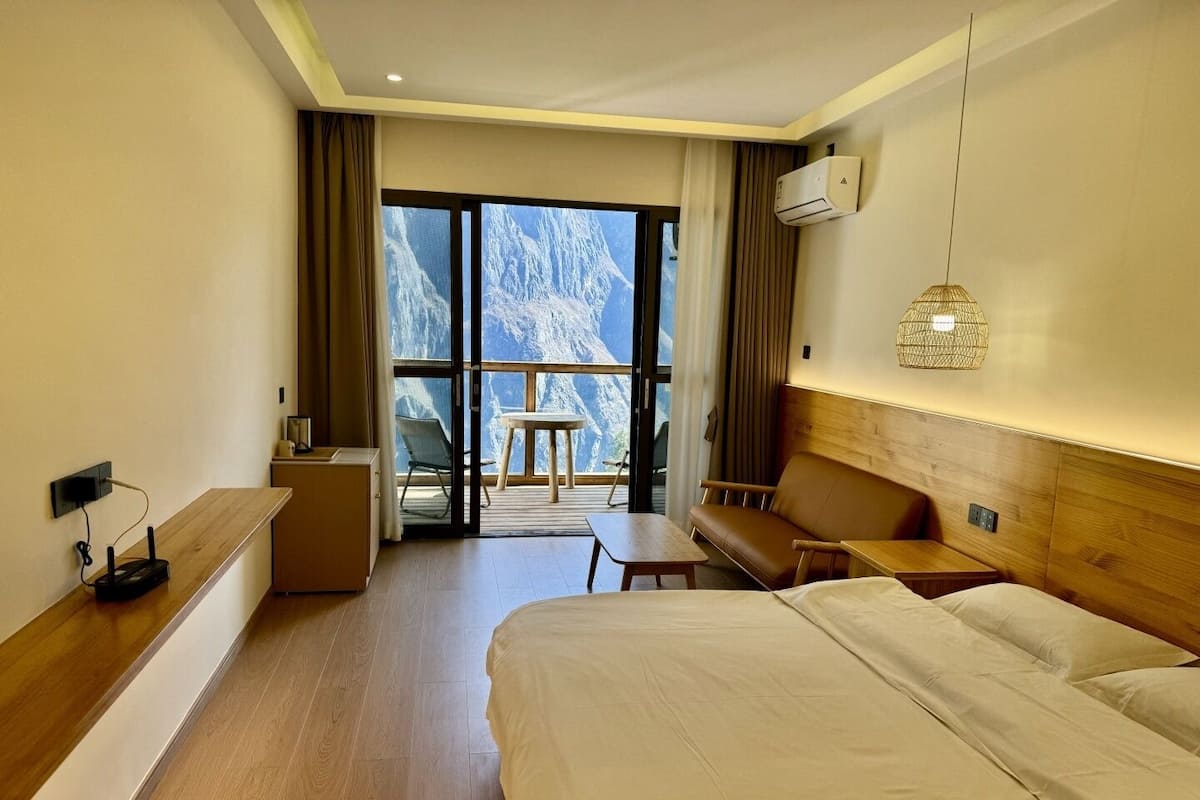 Een hotelkamer met een bed, een bureau, een stoel, een bank en een balkon met uitzicht op bergen.