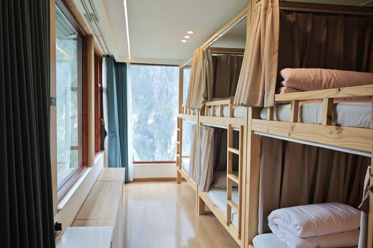 Een slaapkamer met stapelbed, raam, gordijnen en een houten vloer.