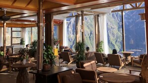 A spacious indoor area with wooden furniture, large windows offering mountain views, and a high ceiling with wooden beams. - Tiger Leaping Half Way Guest House (Deqin)
