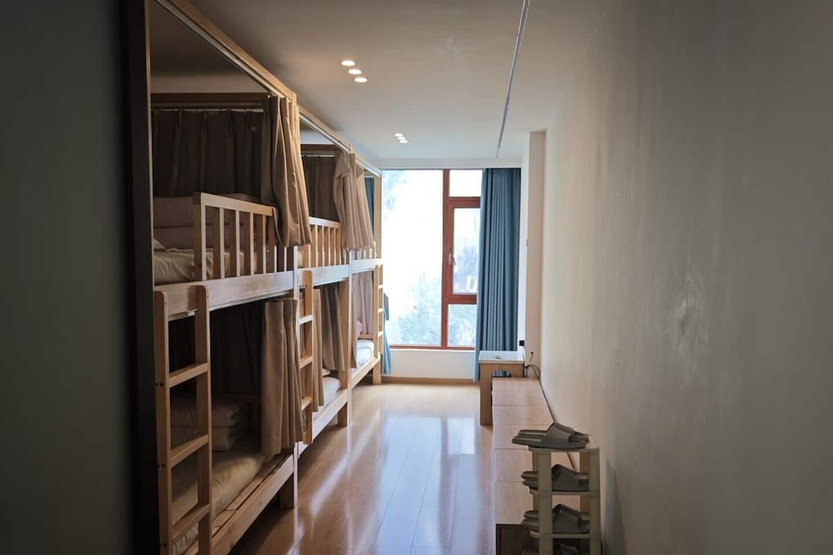 Een kamer met stapelbedden, een raam met gordijnen, een houten vloer en een klein tafeltje met schoenen.