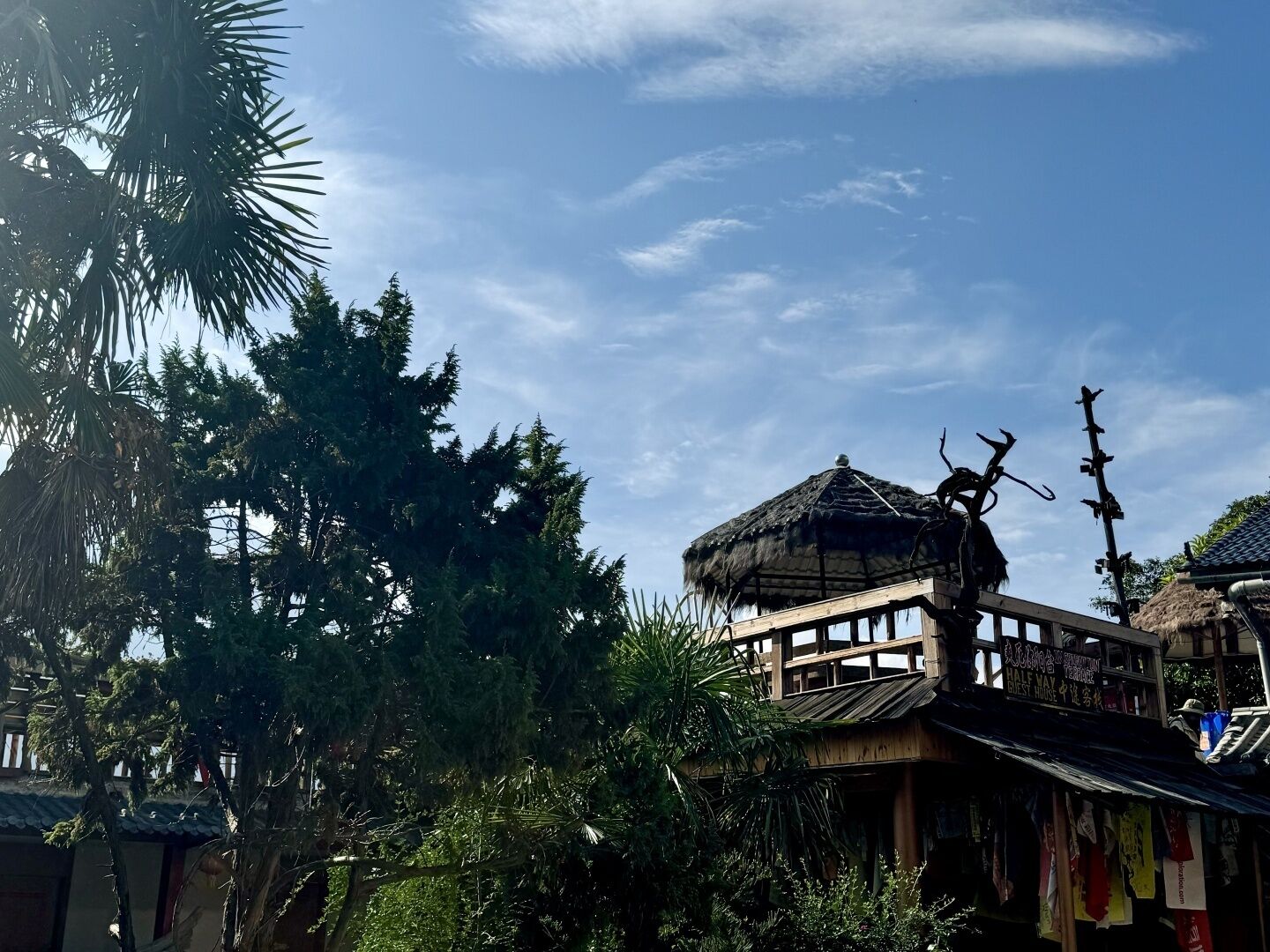 Une construction traditionnelle en bois, dotée d’un toit de chaume, entourée d’une végétation luxuriante et de grands arbres.