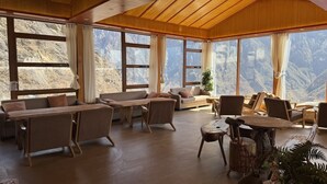 A spacious room with wooden ceiling beams, large windows offering mountain views, a sofa set, and a wooden table. - Tiger Leaping Half Way Guest House (Deqin)