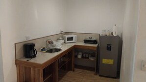 Une cuisine compacte équipée d’un évier, d’un four à micro-ondes, d’une machine à café, d’un réfrigérateur et d’étagères en bois.