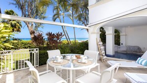 A white outdoor seating area with a glass table and chairs, overlooking a pool and a beach with palm trees. - One Old Trees | Beach Front - Located in  Beautiful Saint James with Private Pool (Saint James)