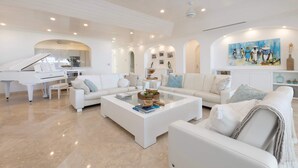 A spacious living room with a white piano, white sofas, and a coffee table. - One Old Trees | Beach Front - Located in  Beautiful Saint James with Private Pool (Saint James)