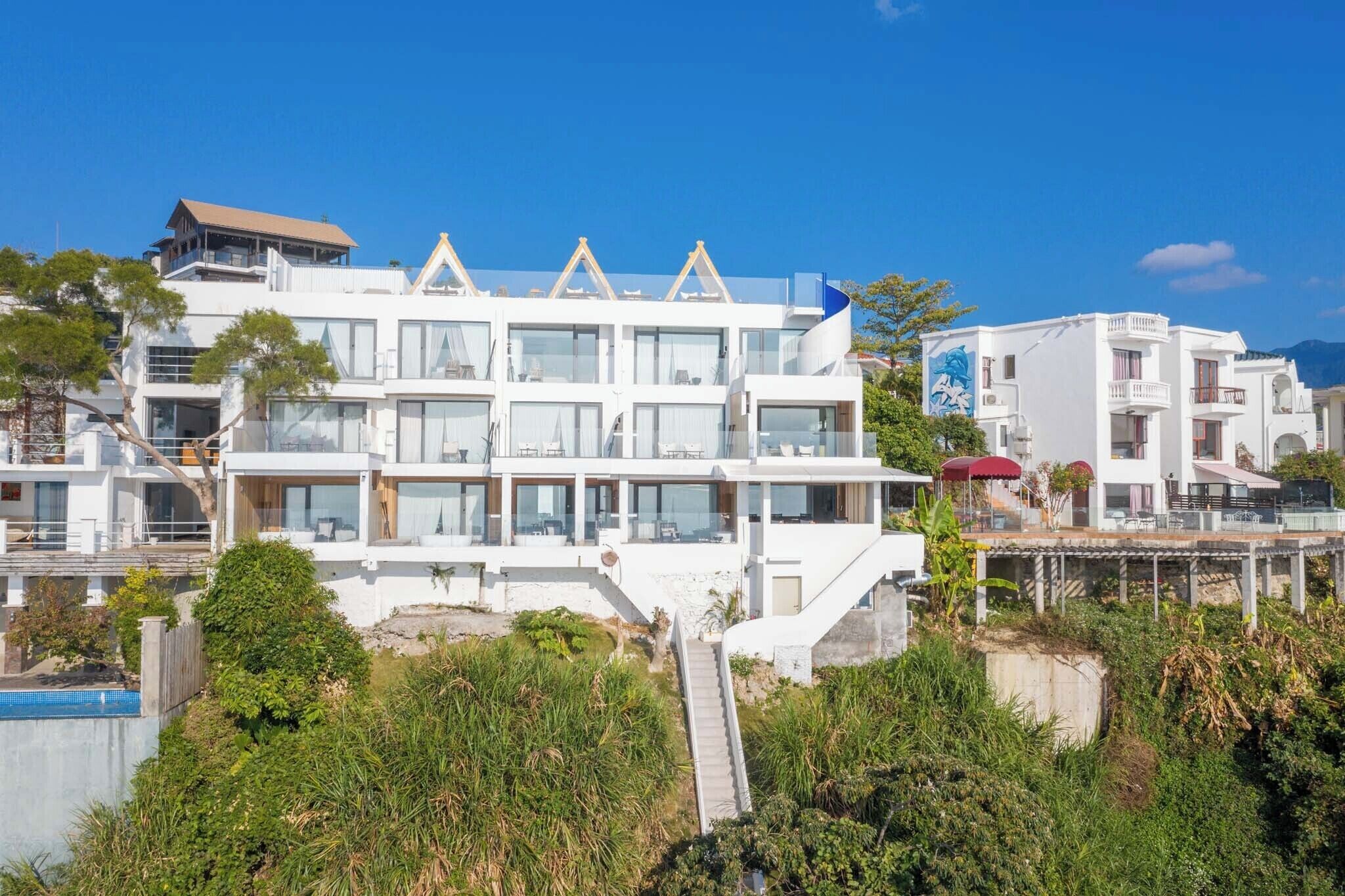 A modern multi-story building with large windows, a staircase leading to the entrance, and a view of the surrounding landscape.